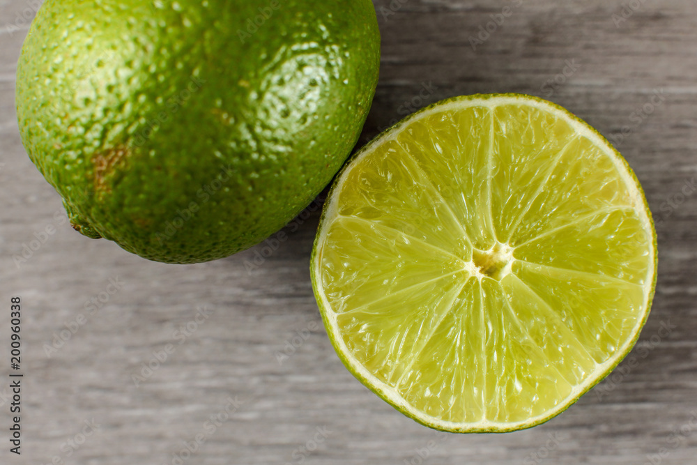 Table top view on green lime cut in half and part of whole one, on a gray wooden table. Table top view on green lime cut in half and part of whole one, on a gray wooden table.