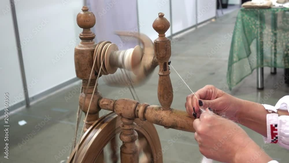 4K view of female hands spin a woolen thread on an old wooden spinning wheel.