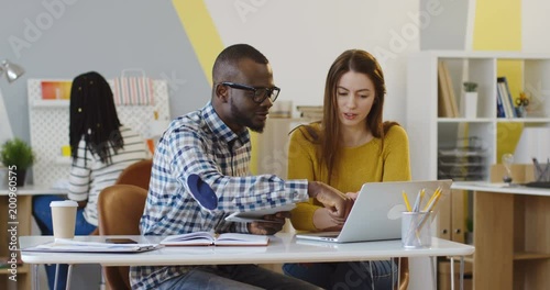 Young multi ethnical team of office workers sitting at the table and working at the laptop computer. Indoor
