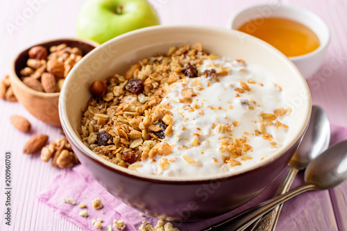 Granola with yogurt in bowl on pink wooden background.