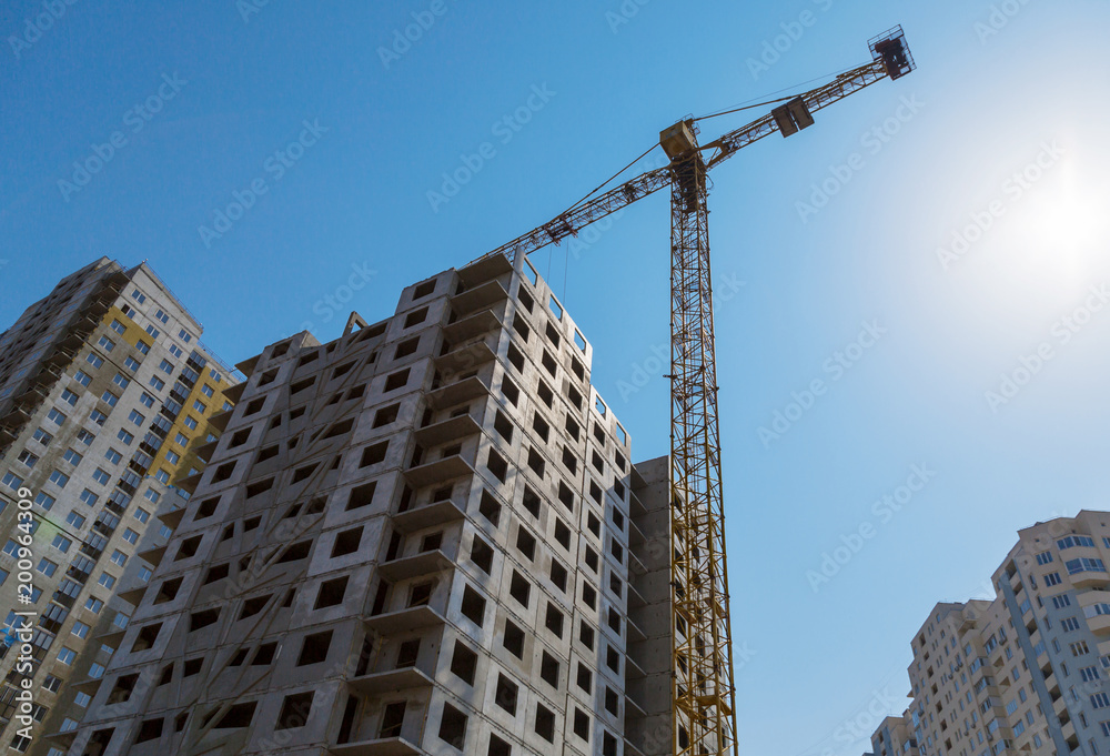 Yellow crane and high building construction site against blue sky