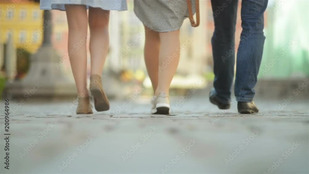 Three Friends Are Walking on Pavement at Midday. They Are Having Fun at This Sunny and Heat Weather. Three Friends Are Walking on Pavement at Midday. They Are Having Fun at This Sunny and Heat Weather.