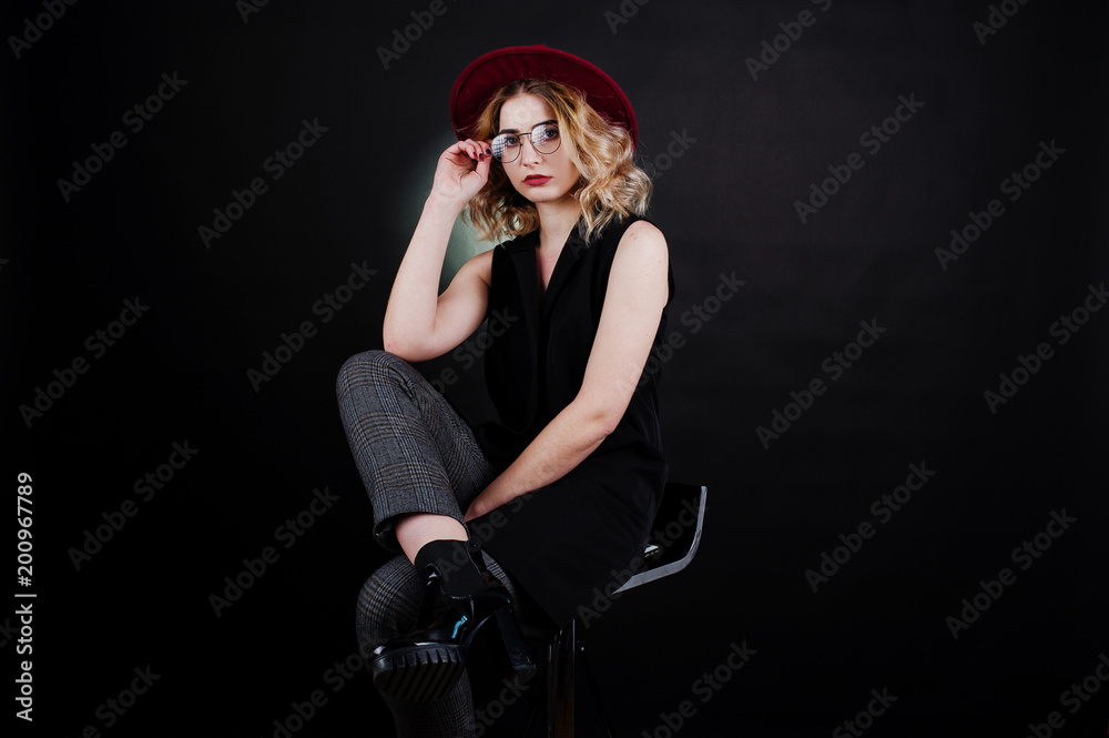 Studio portrait of blonde girl in black wear, red hat and glasses against dark background. Studio portrait of blonde girl in black wear, red hat and glasses against dark background.