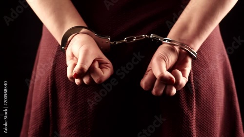 submissive woman wearing a purple dress in leather handcuffs on black background