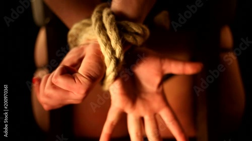 girl has hands bound behind their backs with rope