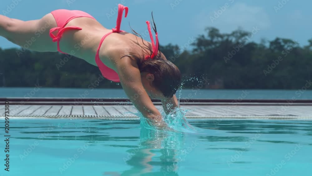 SLOW MOTION, CLOSE UP: Happy female tourist jumps head-first into calm pool during hot tropical summer in Vanuatu. Young woman unwinds on her awesome holiday and dives into refreshing turquoise water.