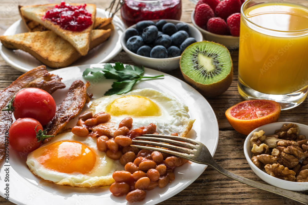 English breakfast served with fried egg, beans, tomatoes, orange juice, bacon and toast with fresh fruits and berries