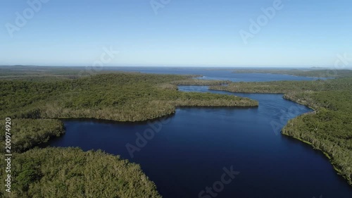 Blue clean freshwater Myall lakes in national park with lush evergreen gumtree woods on shores facing distant pacific ocean.
 photo