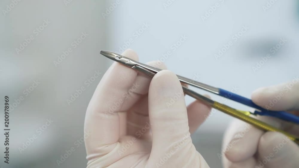 Close up doctor in sterile white gloves examines medical instruments tweezers in the hospital. surgeon dressed in professional clothes examines the clamp in the hands. Close up doctor in sterile white gloves examines medical instruments tweezers in the hospital. surgeon dressed in professional clothes examines the clamp in the hands.