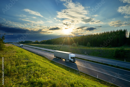 Obraz na płótnie White trucks driving on the highway in the countryside in the rays of the sunset with dramatic clouds w salonie