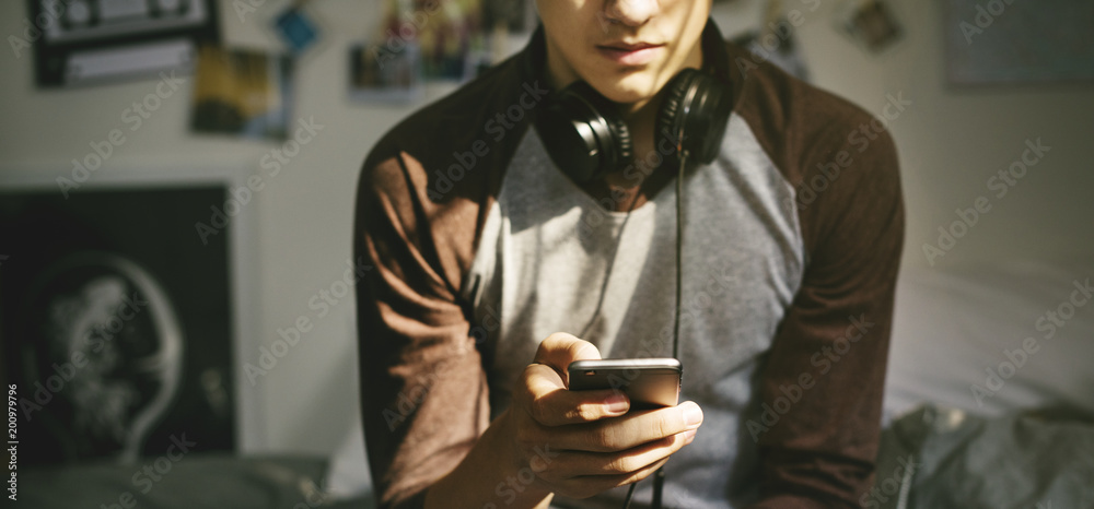Φωτογραφία Teenage boy in a bedroom listening to music through his smartphone