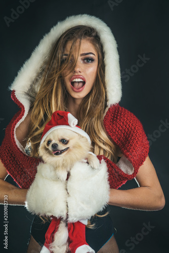 Christmas woman. Santa girl and dog in Christmas dressed as Santa Claus. New year, holiday, celebration concept. Holiday makeup. Cute happy woman in white fur gloves with dog on black background.