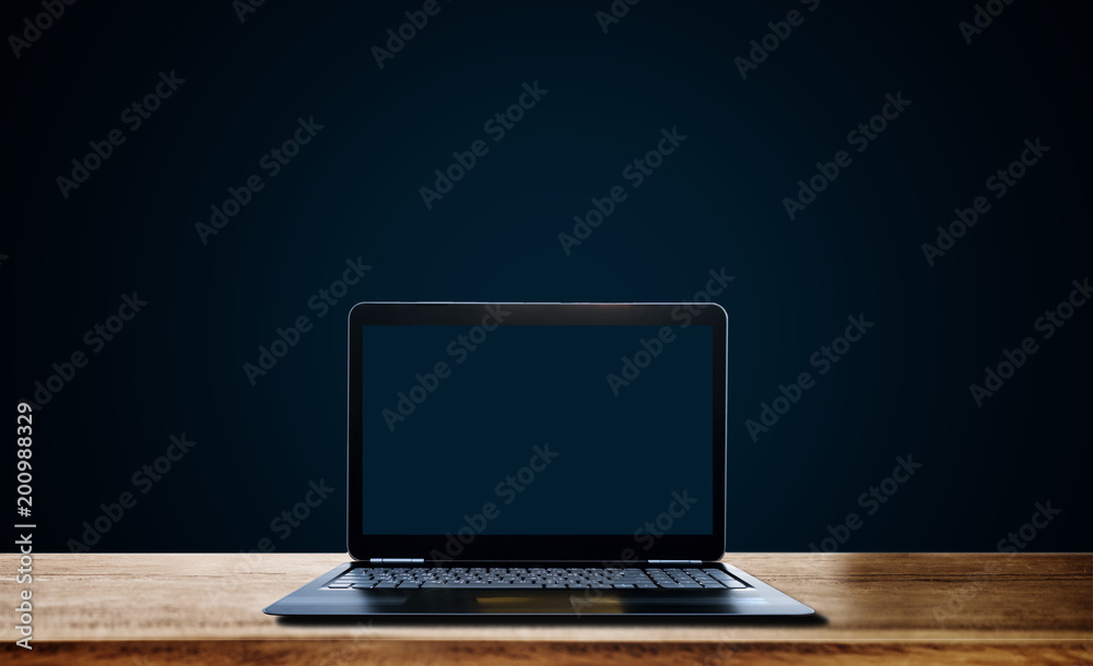 Computer laptop empty blue screen on wooden desk, on dark blue background Computer laptop empty blue screen on wooden desk, on dark blue background