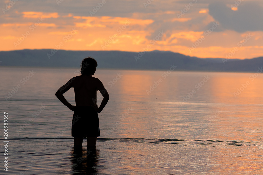 silhouette of a man who stands in the water and looks towards the sunset