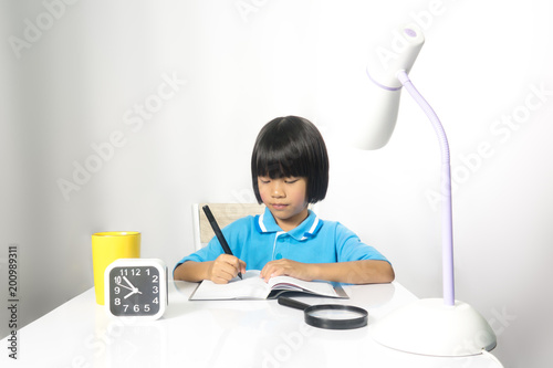 Soft cute child writing and working on work desk. Asian child girl is active and wisdom for working. She sitting on chair on white gray fabric background photo