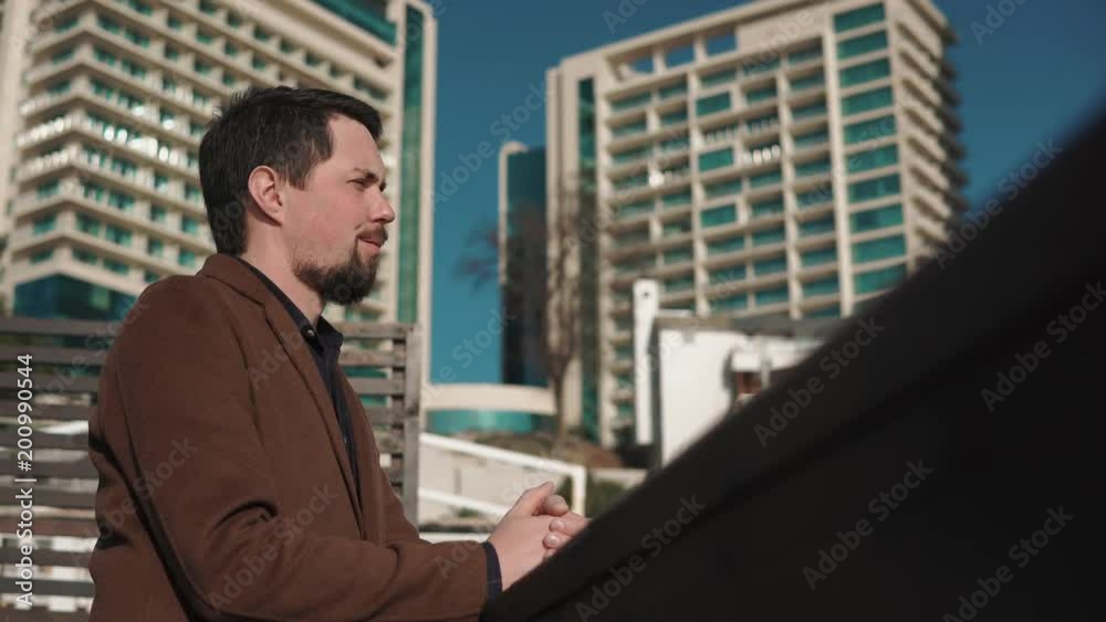 Handsome man is resting and enjoying urban landscape in daytime. He is looking in distance and thinking, high modern buildings are in background Handsome man is resting and enjoying urban landscape in daytime. He is looking in distance and thinking, high modern buildings are in background