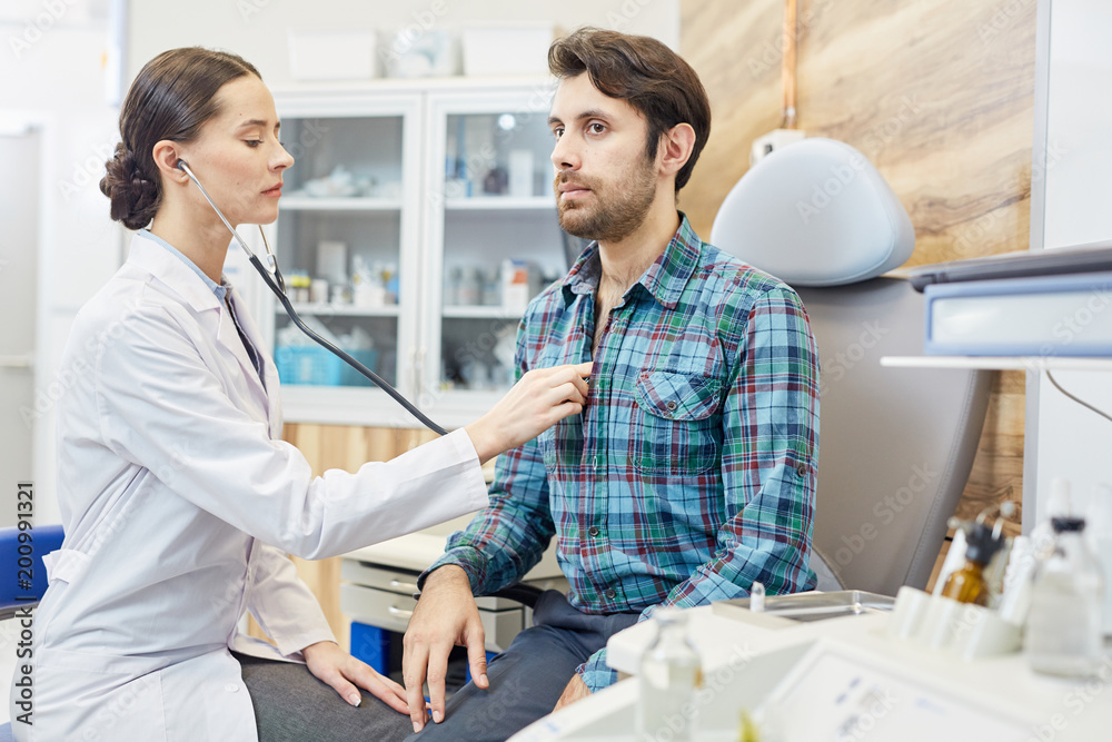 Fototapeta premium Female doctor examining her patient with stethoscope