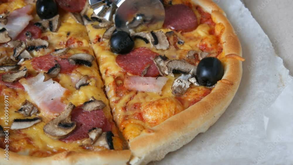Hand cut a piece of a Big Italian pizza with black olives, bacon, salami and cheese close up Hand cut a piece of a Big Italian pizza with black olives, bacon, salami and cheese close up