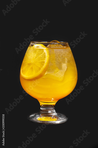 Single-colored cocktail, yellow refreshing in low plump glass with ice cubes and a round slice of orange, lemon with the taste of pineapple, melon, peach, apricot. Side view Isolated black background