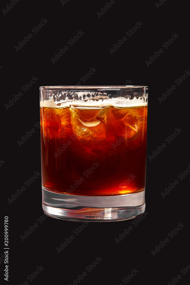 Single-colored transparent cocktail, brown, red refreshing carbonated with foam in a low glass with ice cubes and cola taste. Side view. Isolated black background. Drink for the menu Single-colored transparent cocktail, brown, red refreshing carbonated with foam in a low glass with ice cubes and cola taste. Side view. Isolated black background. Drink for the menu