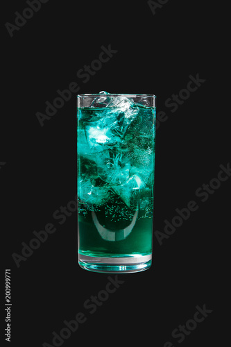 Single-colored transparent cocktail, blue, blue refreshing carbonated in a high glass with ice cubes. Side view. Isolated black background. Drink for the menu restaurant, bar, cafe