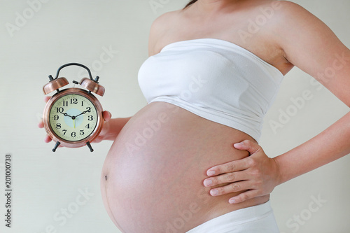 Pregnant woman with big belly in white underwear holding vintage alarm clock. Pregnancy waiting baby concept.