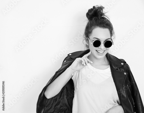Portrait of young beautiful brunette woman girl model with nude makeup wearing summer hipster biker leather jacket clothes in sunglasses posing near wall. Going crazy