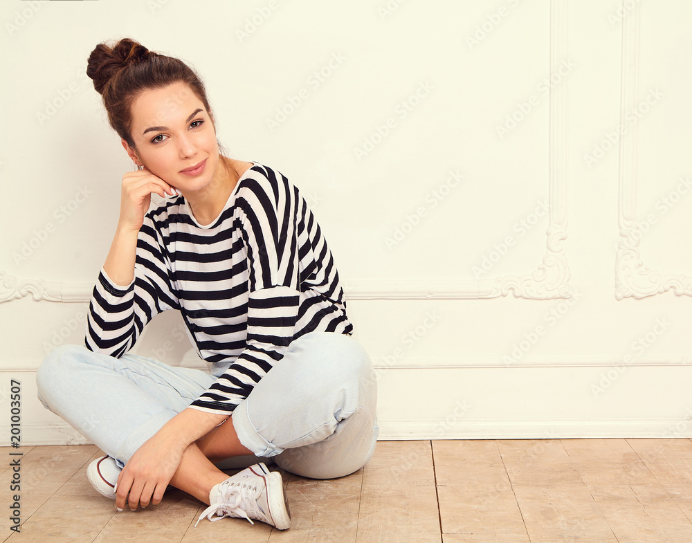 Portrait of young beautiful brunette woman girl model with nude makeup in summer hipster clothes posing near wall. Sitting on the floor Portrait of young beautiful brunette woman girl model with nude makeup in summer hipster clothes posing near wall. Sitting on the floor