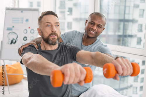 Physical strength. Serious adult man holding dumbbells in front of him while exercising