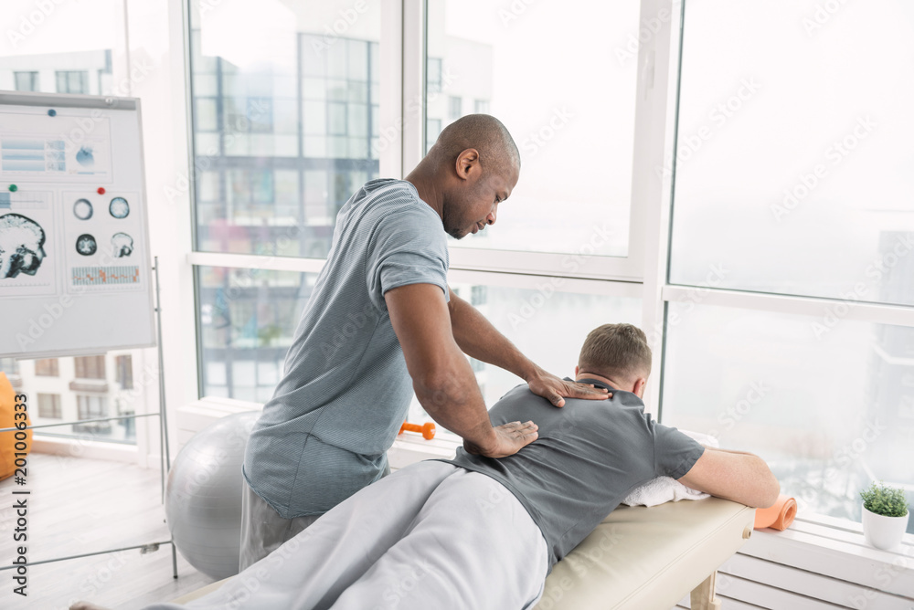 Professional orthopedics. Skillful nice orthopedist working with his patient while doing a massage for him Professional orthopedics. Skillful nice orthopedist working with his patient while doing a massage for him