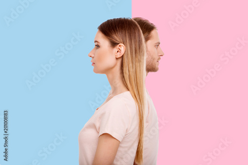 Diverging views. Pleasant young woman and her boyfriend standing in a line but looking into different directions while posing against blue and pink backgrounds respectively photo