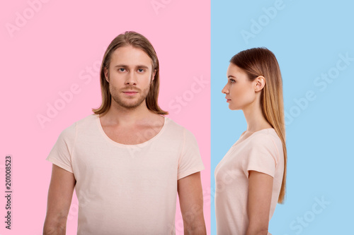 My eyes on you. Pretty young woman standing sideways and facing her boyfriend while the man standing against a pink background and looking at the camera