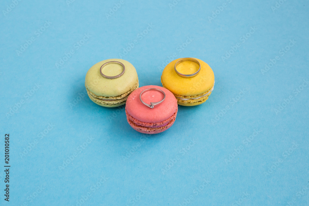 Wedding rings on macarons or macaroons on turquoise background from above, colorful almond cookies, pastel colors, top view Wedding rings on macarons or macaroons on turquoise background from above, colorful almond cookies, pastel colors, top view