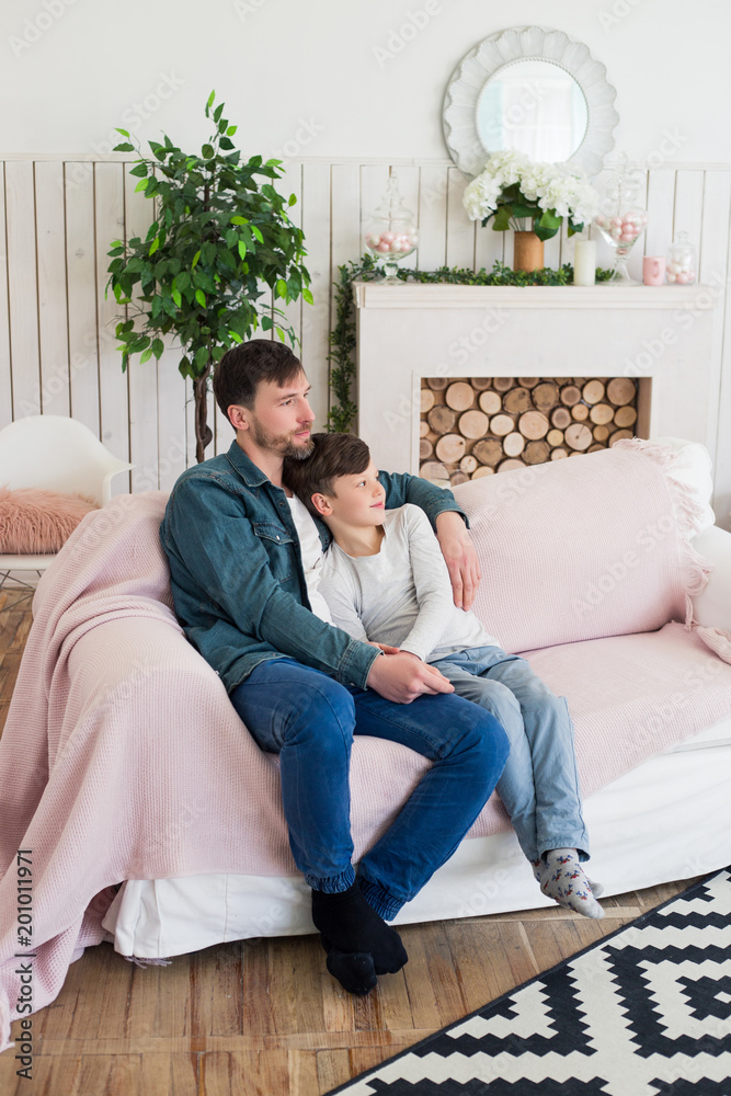 Teaching a boy to be a man is the primary job of a father! Full length photo of the dad and his son sitting on the couch and giving hugs to each other.