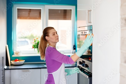 Young woman in rubber gloves cleaning oven