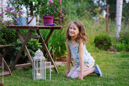 happy dreamy kid girl playing in summer garden, decorated with lantern light and candle. Blooming flowers on background.