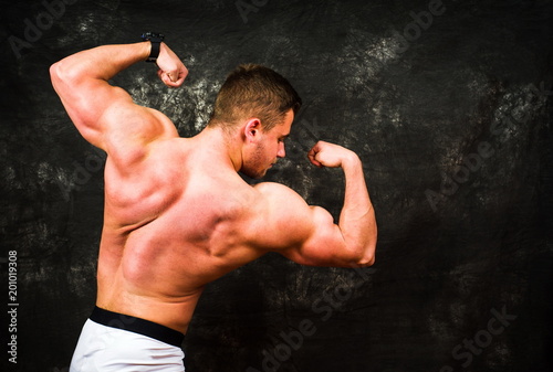 Bodybuilder flexing muscles against dark background © creativefamily
