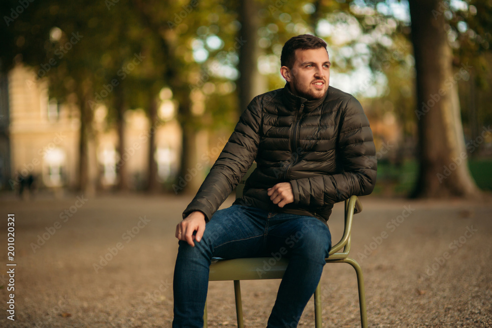 Handsome man sits in the middle of the park in khaki stool Handsome man sits in the middle of the park in khaki stool