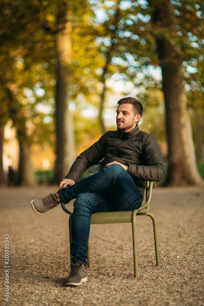 Handsome man sits in the middle of the park in khaki stool Handsome man sits in the middle of the park in khaki stool