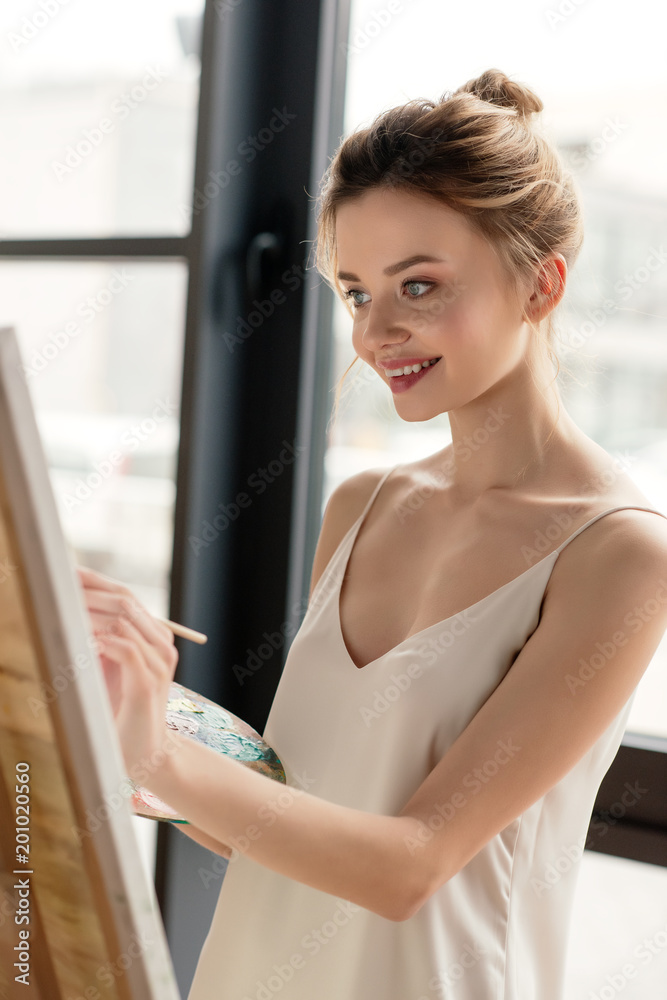 beautiful smiling young artist painting picture in studio