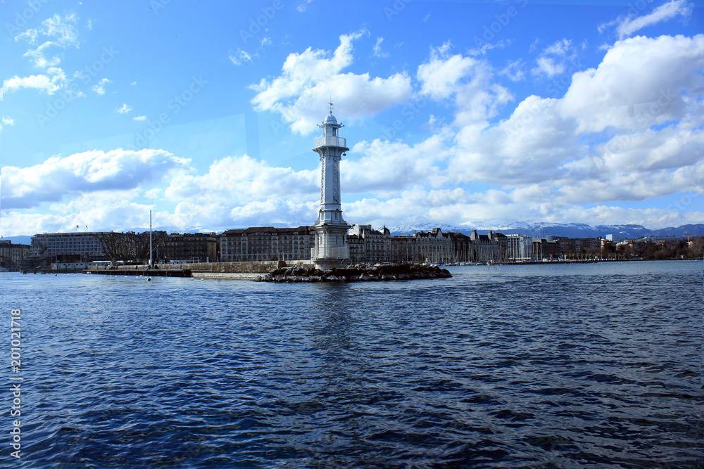Sunny day in Geneva with white lighthouse in the middle of lake. Blue background. Swiss Alps there