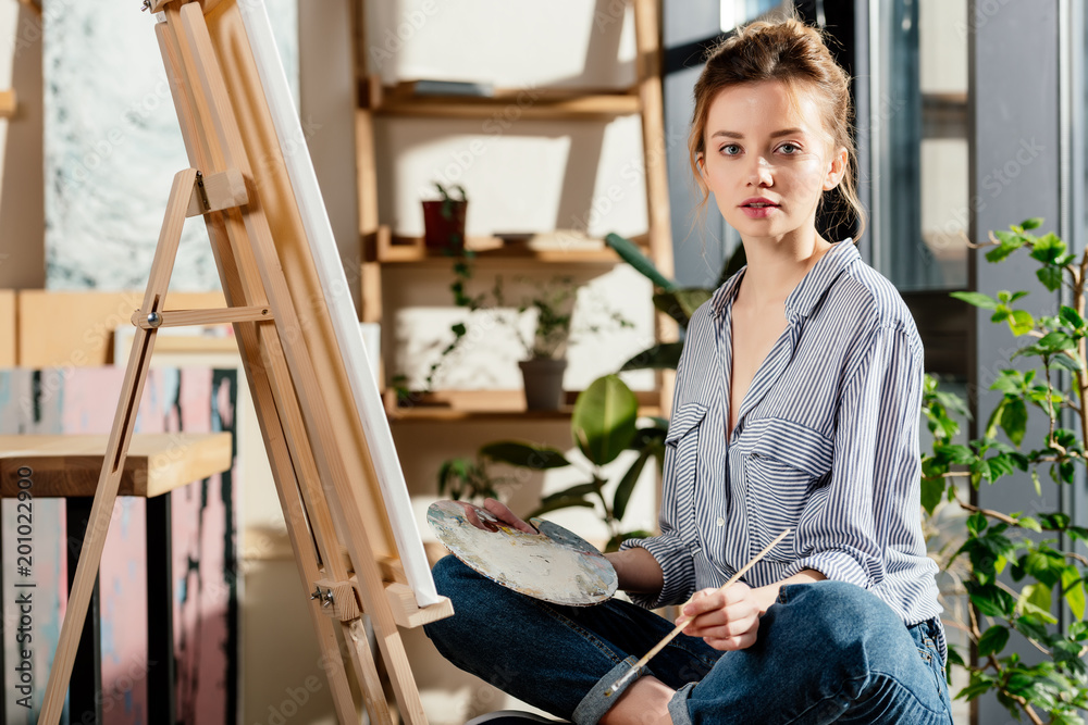 attractive female artist sitting on bench and holding palette and paintbrush attractive female artist sitting on bench and holding palette and paintbrush