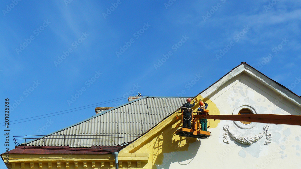 Builders on the crane paint with yellow paint an old building. A minimalistic photograph. Blue sky. space for text, copy space.