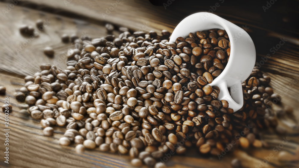 Naklejka premium Coffee beans are poured from a Cup on a wooden background. Copy space for text. Dark background.