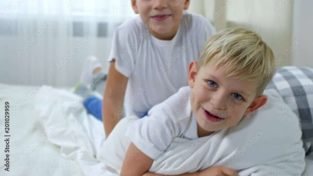 Close up shot of two brothers of primary school age lying on bed and fighting with pillows Close up shot of two brothers of primary school age lying on bed and fighting with pillows