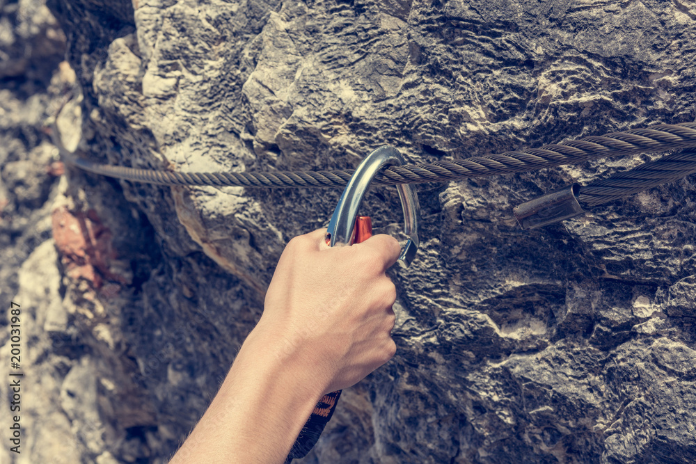 Closeup of female climber attaching via ferrata set to steel cable.