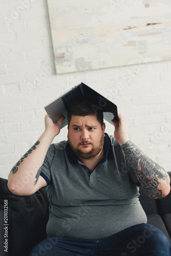 handsome man holding laptop on head and looking away at home