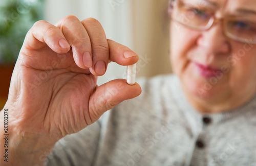 Senior Woman Taking Medication  holding pill in hand  looking though glasses. Close-up 