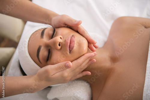 Facial procedure. Attractive nice woman lying with her eyes closed while enjoying facial massage