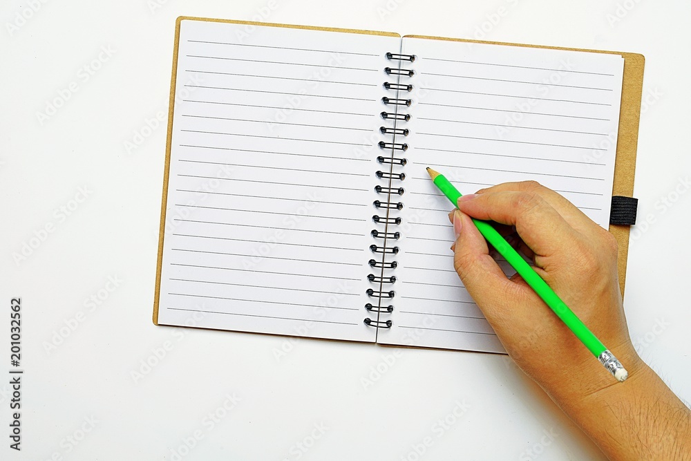 Top view and copy space, A hand holding a green pencil, trying to write something on a book, that was opened on white table.